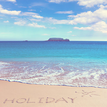 HOLIDAY insctiption under the sun drawing on wet beach sand with the turquoisesea and the island on background