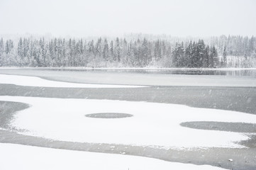 Snowfall over freezing lake.
