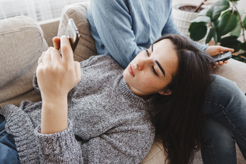 Couple in living room using smart phones. Young people chatting online.