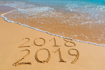 2018 2019 inscription written in the wet yellow beach sand being washed with sea water wave