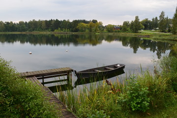 Beautiful landscape. Wooden bridge with boat. Lake, forest, shore, sky. Reflection in water.