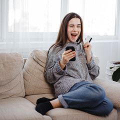 Excited woman discovering offer shopping at online store with credit card and phone at home. Technology, electronic business, sale concept
