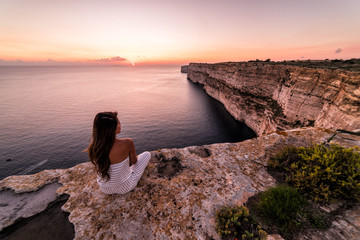 Woman overlooks the famous Ta Cenc Cliffs at sunset.  These cliffs on the island of Gozo overlook the Mediterranean Sea.  Country of Malta.