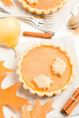 Pumpkin pie with cinnamon and cookies on gray napkins on white wooden background with autumn yellow leaves.