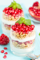 Pomegranate parfait - sweet organic layered dessert with granola flakes, yogurt and red ripe fruit seeds.