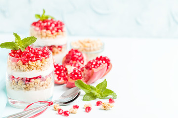 Obraz na płótnie Canvas Pomegranate parfait - sweet organic layered dessert with granola flakes, yogurt and ripe fruit seeds.