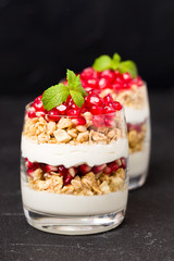 Pomegranate parfait - sweet organic layered dessert with granola flakes, yogurt and fruit seeds on black background.