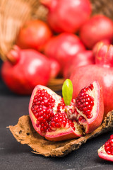 Ripe red pomegranates in wicker basket and seeds in spoon closeup photography on black background.
