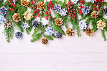 Beautiful Christmas composition of fir branches decorated with bows, pine cones and red berries. Place for text on a light background.