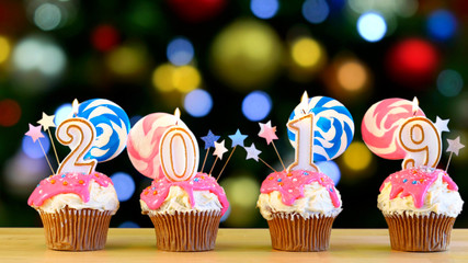 2019 Happy New Year's candy land lollipop drip cupcakes against bokeh Christmas lights background.