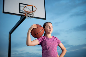 Girl holding a basketball at an outdoor court
