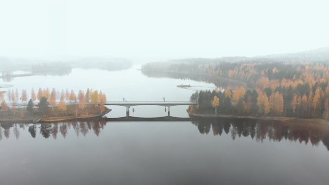 Aerial, drone shot, flying towards a bridge, surrounded by mist and autumn colors,, on a foggy, misty and cloudy, fall day, at lake Pielinen, in Nurmes, North Karelia, Finland