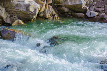Fototapeta na wymiar Clear river with rocks leads towards mountains, small waterfall