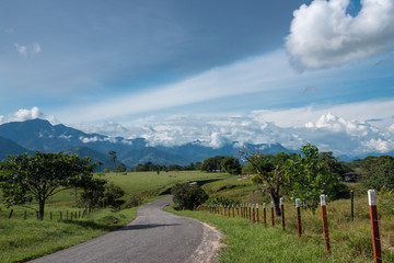 Fototapeta na wymiar Highway between green landscape with mountains in the background with blue sky among clouds. Colombia