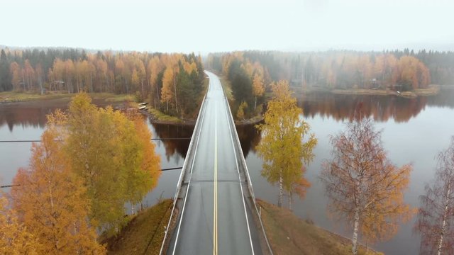 Aerial, decreasing, drone shot, above a bridge, surrounded by mist and autumn colors,, on a foggy, misty and cloudy, fall day, at lake Pielinen, in Nurmes, North Karelia, Finland