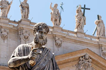 Statue of St. Peter in the Vatican holding the key to heaven, with St. Peter's Basilica in the background and statues of the other apostles 