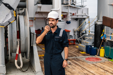 Marine Deck Officer or Chief mate on deck of vessel or ship . He holds VHF walkie-talkie radio in...