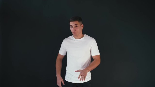 Serious young man stands and looks on camera. Then he starts to move his hands and dance. He is bouncing around. Hands moves up and down. He has fun. Then guy smiles. Isolated on black background