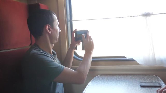 man traveler taking pictures on a smartphone and smiling through the pictures via social media. slow motion video. uploading photo using cell phone while riding home by train wagon compartment. train