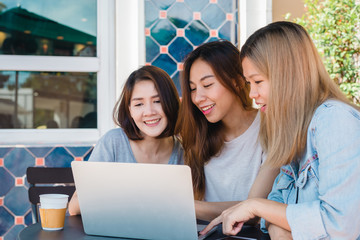 Group of beautiful smart business freelance Asian women in smart casual wear working together on laptop or computer while sitting on table in creative office or cafe.