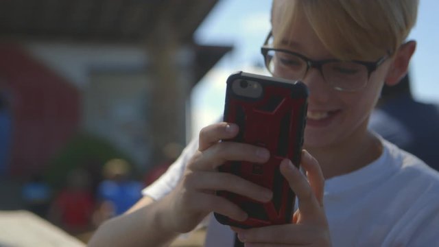 Cute tween boy outside texts on his phone and giggles to himself