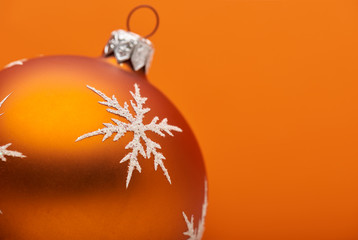 An orange Christmas bauble decoration close up adorned with a silver white snow flake on an orange...