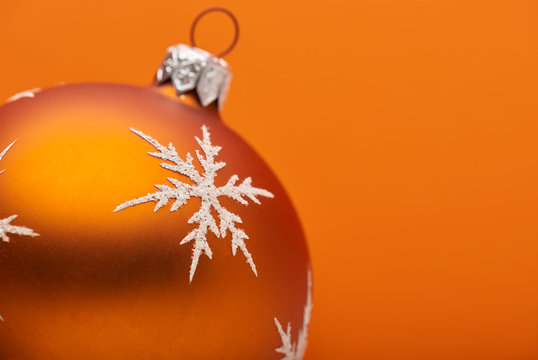 An orange Christmas bauble decoration close up adorned with a silver white snow flake on an orange background with room for custom text.
