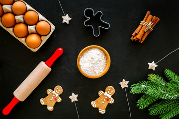 Fototapeta na wymiar Cook homemade gingerbread cookies for New Year party. Rolling pin, eggs, flour, cinnamon near gingerbread man and spruce branch on black background top view