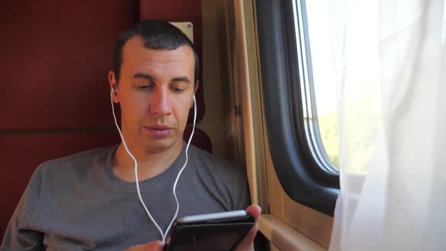 man listening to the music on the train rail car coupe compartment travel. slow motion video. man with a smartphone lifestyle at the window of a train in a car travel internet social media web. man