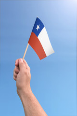 Hand holding Chile flag high in the air, with a clear blue sky