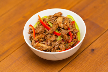 Noodles with pork, vegetables and sesame. On a wooden table.