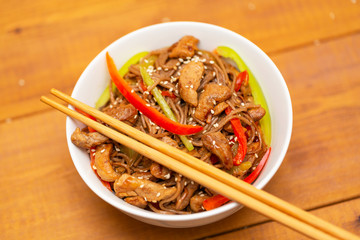 Noodles with pork, vegetables and sesame. On a wooden table.