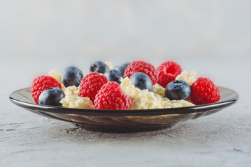 Cottage cheese with fresh raspberries and blueberries in a plate for a healthy breakfast with ripe berries. A natural healthy product.