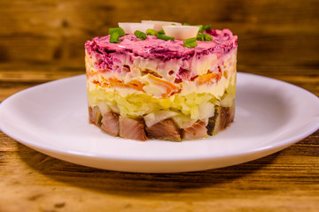 White plate with russian traditional new year salad herring under fur coat on wooden table