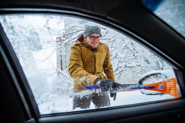 smiling man scrapping car of snow and ice.