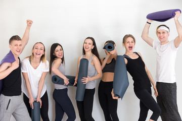 Group of sportive athletic people girls and guys standing in row holding yoga mats have fun...