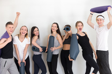 Group of sportive athletic people girls and guys standing in row holding yoga mats have fun together laughing smiling feels good, satisfied excited after sport training fitness workout at gym studio