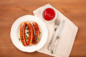 An overhead photo of a plate of fried sausages with ketchup, shot from above on a dark rustic wooden background with copy space