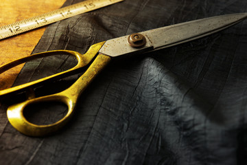 Measuring and cutting textile or fine fabric. Work table of a tailor. Gold scissors and black fabric.