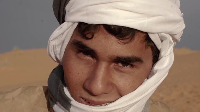portrait shot of Moroccan young man in sahara desert of Morocco with his tradionnel looking. The male lives as nomad in the desert.