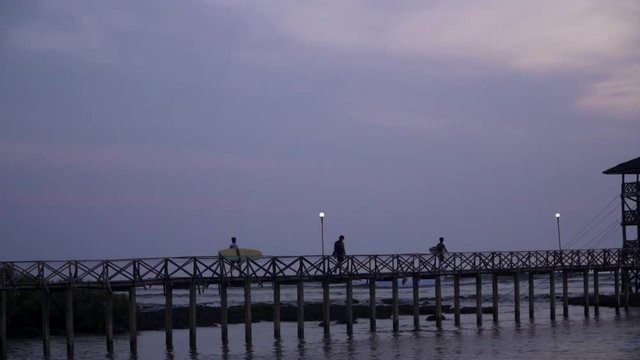 Tracking shot of surfers walking across the Cloud9 boardwalk with the sun low and out of frame, silhouetted against a cloudy sky, filmed in UHD 4K