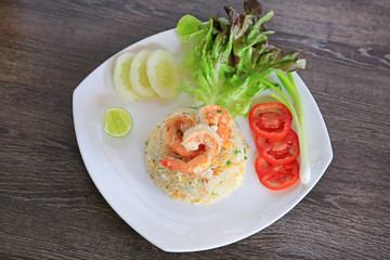 Thai style Fried rice with shrimp on white plate against wood table. Food decoration with vegetables.