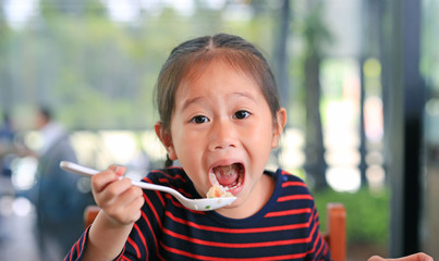 Smiling little Asian child girl sitting at the cafe and eating food with looking straight