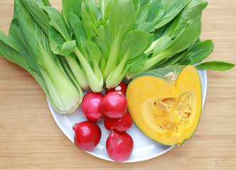 Fresh vegetables on plate against wooden background
