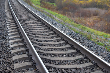 Railway rails and ties on train track on autumn grass background.