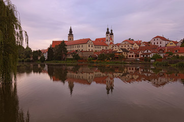 Naklejka na ściany i meble Scenic view of Telc castle, lake, Name of Jesus Church and tower of the Church of St. Jakub. Buildings are reflected in the water. Early morning landscape. A UNESCO World Heritage Site
