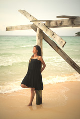 Fototapeta na wymiar Young asian Vietnamese woman leaning against an old wooden pier on beach posing with sea in background