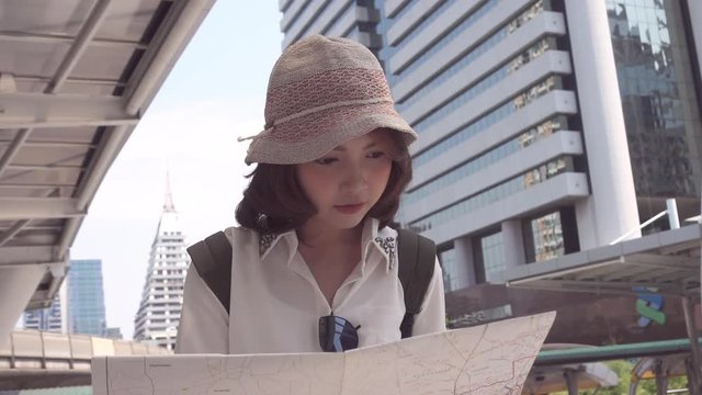 Slow motion - Cheerful beautiful young Asian backpacker woman direction and looking on location map while traveling at Bangkok, Thailand. Lifestyle backpack tourist travel holiday concept.