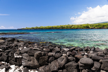 View of kealakekua bay on Hawaii's Big Island, looking from Puuhonua Historical Park. Crystal blue-green water in the bay; coastline in the background, black Volcanic rock in foreground.