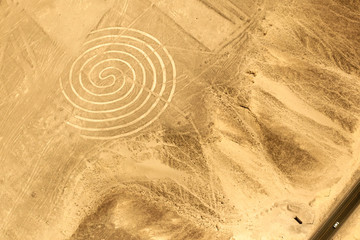 The size and scale of one of the spiral patterns found on the floor of the Nazca Plain is emphasised by the tiny car driving on the highway passing the site.